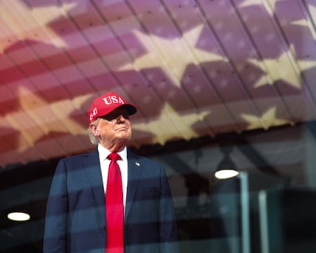 Man in red tie and Maga hat looks out of window at airport