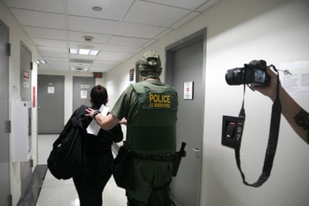 a federal agent with hands on a person’s back in an office hallway