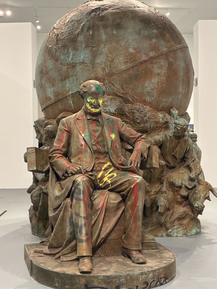Bronze statue of man sitting, with earth looming behind him.