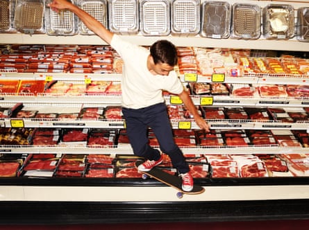 A man leaps on a skateboard by a meat counter in a supermarket