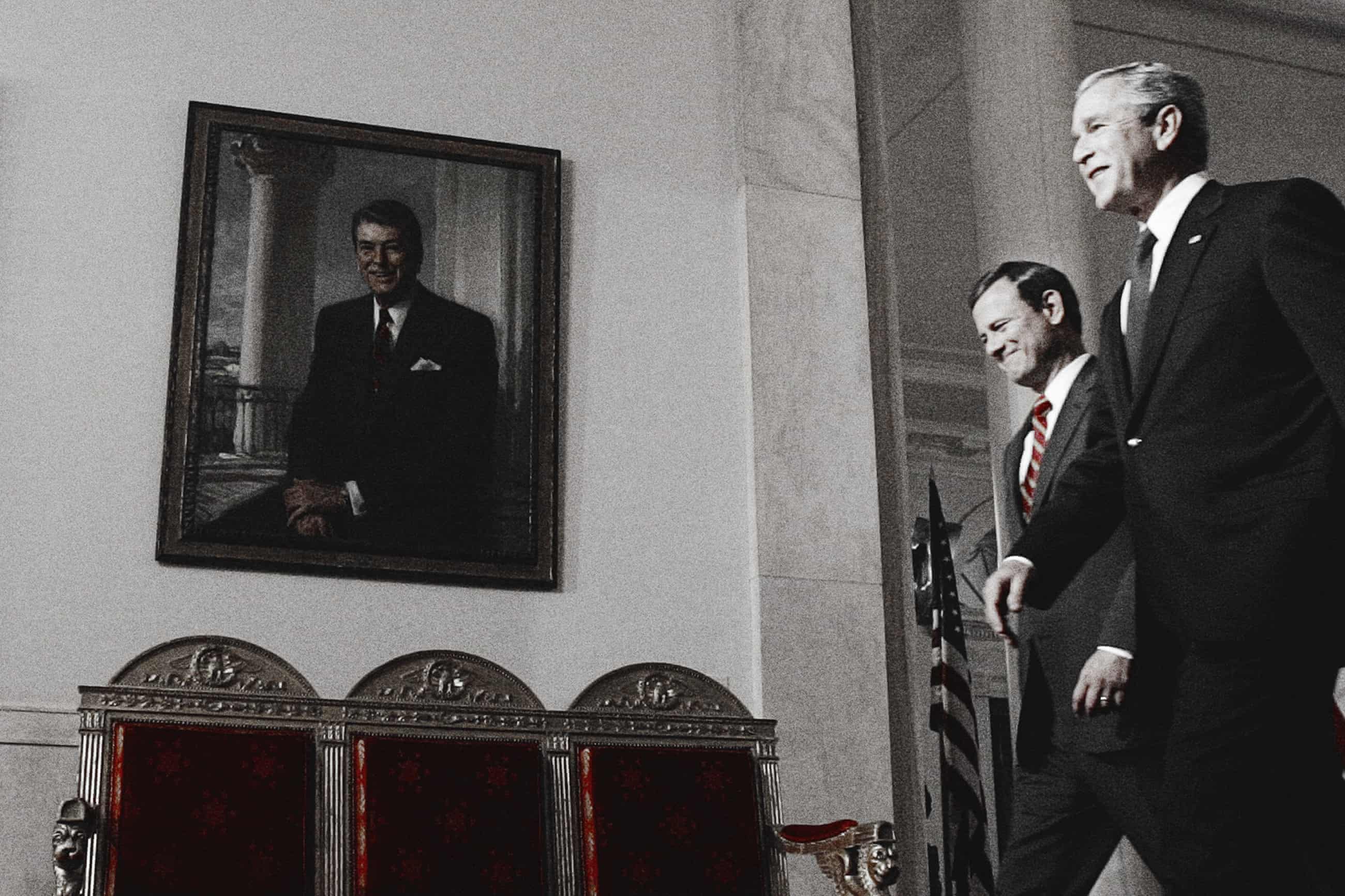 Two men in suits walk through a corridor next to a portrait of Ronald Reagan