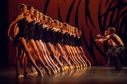 A line of female ballet dancers with one leg stretched forward, and two male dancers in front of them