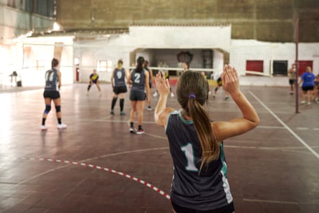 A volleyball player raises both hands behind teammates during a match on an indoor court