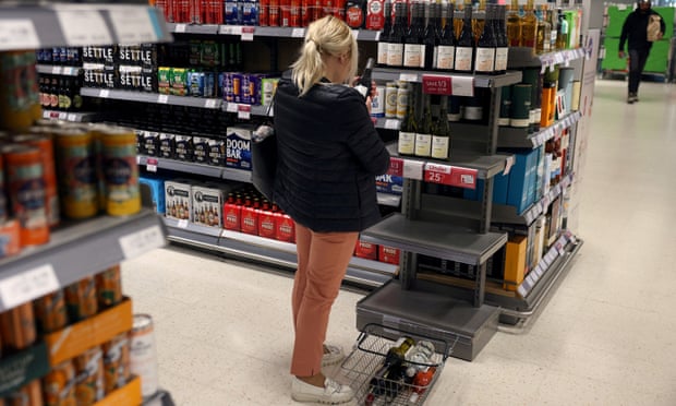 A woman looks at wine bottles displayed on a shelf in a supermarket