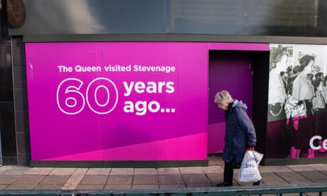 Older person walks in front of hoarding with picture of Queen visiting Stevenage 60 years ago