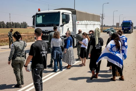 Israeli border guards and right-wing protesters stand by as Jordanian trucks carrying humanitarian aid supplies pass by while arriving on the Israeli side of the Kerem Shalom border crossing on 16 April.