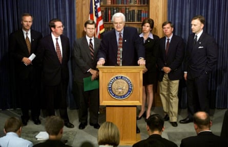 a line of men stands behind a man speaking at a lectern