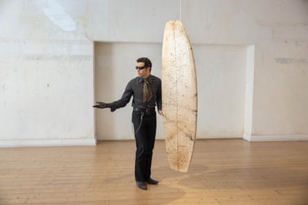 Lecacheur stands beside a surfboard that is dangling from the roof of the apartment