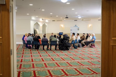 A gathering of people sit on chairs in a circle in the middle of a large room inside a mosque