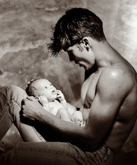 Photograph of muscly man without a top on cradling a very young baby