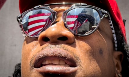 A young Black man wears sunglasses with a flag reflected in them.