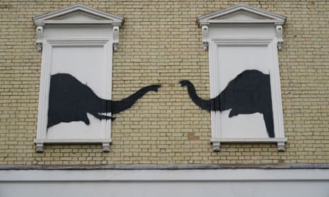 Black spraypainted elephant heads face each other from two white-painted blocked-out windows, with their trunks reaching out towards each other