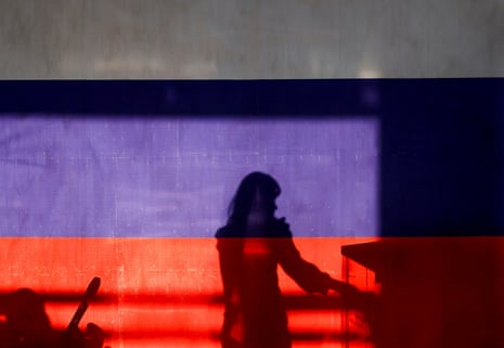A woman is silhouetted behind a banner in the colours of the Russian flag at a polling station