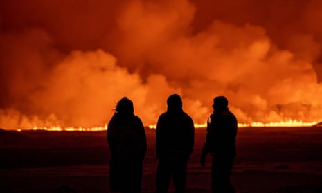 People watch as the night sky is illuminated caused by the eruption of a volcano in Grindavik on Iceland's Reykjanes Peninsula, Monday, Dec. 18, 2023.