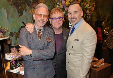 Cox with Elton John and David Furnish in 2015, with Cox’s shoes behind them.