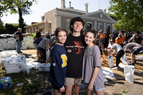 Macey Barber, Sam Deola and Cleo Oberin pose in front of the Echuca town hall in front of other volunteers as they prepare sandbags