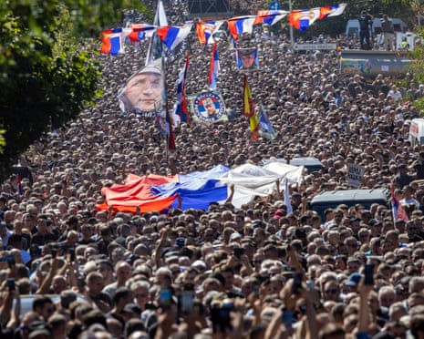 People gathered for the funeral procession wave a flag showing the former Bosnian Serb army commander Ratko Mladić on the day of his funeral.