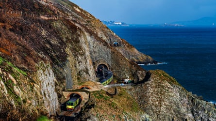 Train emerges from tunnels in headland by the sea