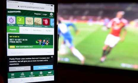 A betting app on a mobile phone held in front of televised football.