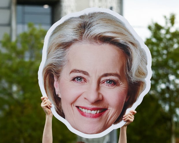 A person holding a large cutout of Ursula von der Leyen's head