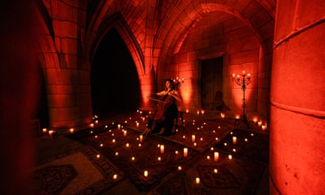 Candles surround a musician in a an old vaulted space lit in red