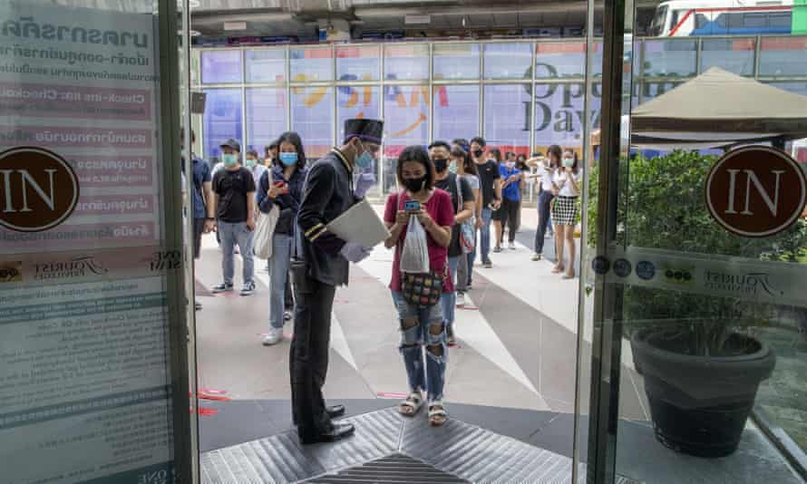 A woman displays her phone to doorman, to conform using a mobile application to help contact-tracing at the entrance to the upmarket shopping mall Siam Paragon in Bangkok, Thailand, on Sunday.