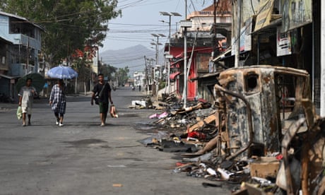 People walk past a burnt vehicle and rubble in Churachandpur in violence-hit areas of the north-eastern Indian state of Manipur on 9 May.
