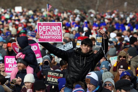 A crowd of demonstrators mass witha Hspanic-looking boy on someone's shoulders holding a rosary and a placard saying Defund Planned Parenthood
