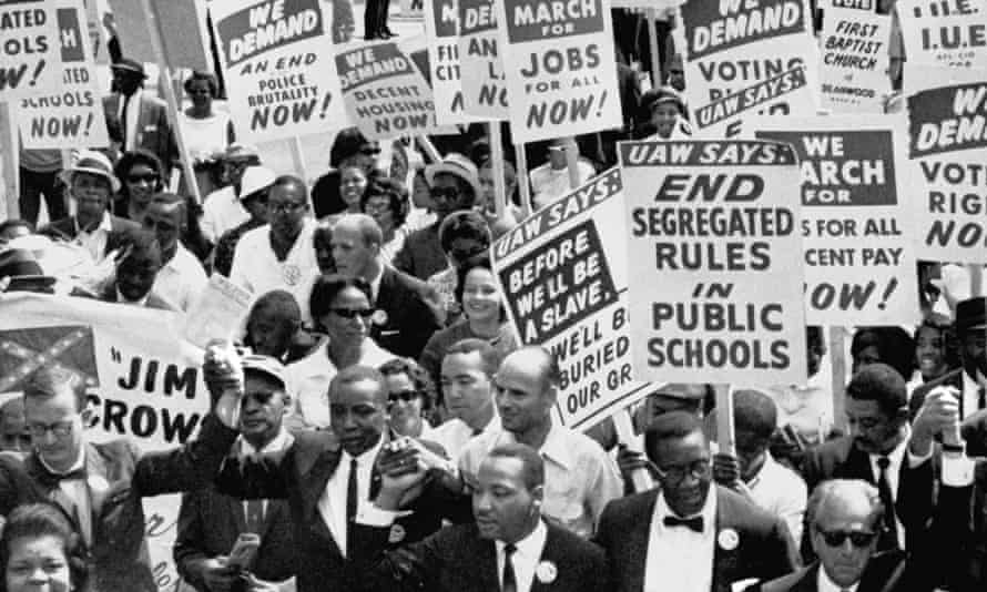Dr. Martin Luther King, Jr., third from left, marches in a line of men with arms linked.