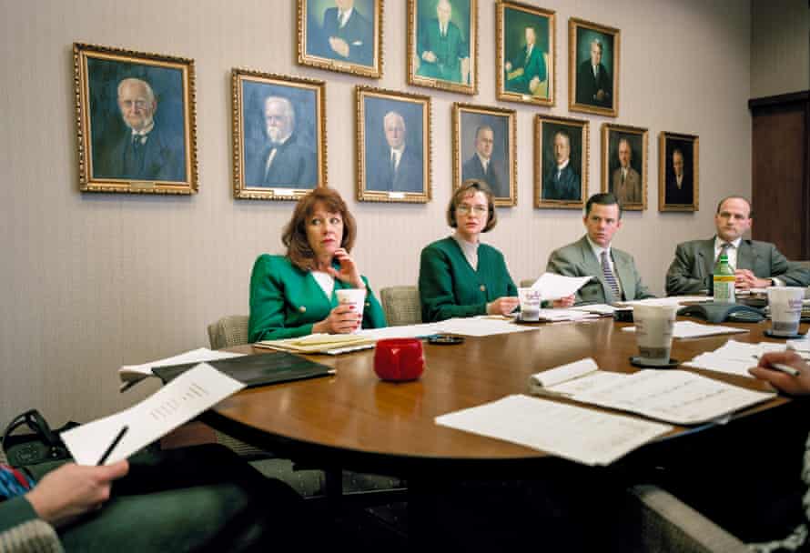 Office workers sitting round a big desk in front of a wall with lots of portraits on it