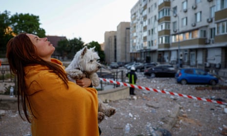 A woman with a dog looks at her apartment building damaged during a drone strike.