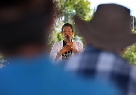 Deb Haaland speaks into a microphone outdoors, seen between two blurred onlookers
