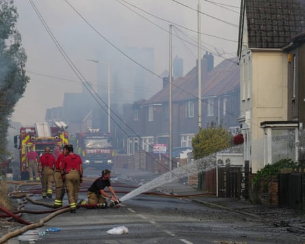 A firefighter holds a hose spraying water on a house