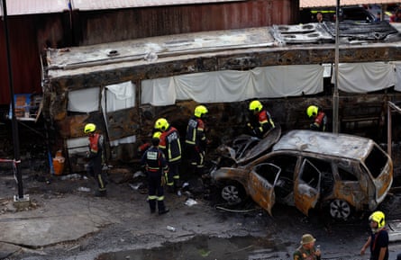 Rescue workers inspect the wreckage of the burned-out bus and a car.