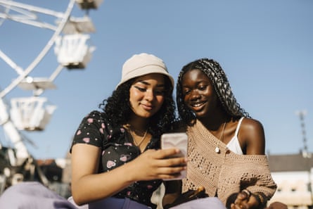 Smiling female friends using smart phone against clear sky on sunny day