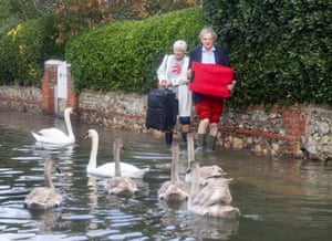 Um casal carrega malas enquanto passa por cisnes nas enchentes da maré alta em Bosham, em West Sussex. Alertas meteorológicos amarelos para chuva estão em vigor para o resto da semana, antes da tempestade Ciarán atingir o sul do Reino Unido na quinta-feira.
