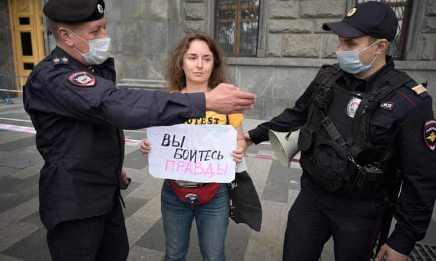 Police officers detain a journalist who holds a placard reading ‘You are afraid of the truth'