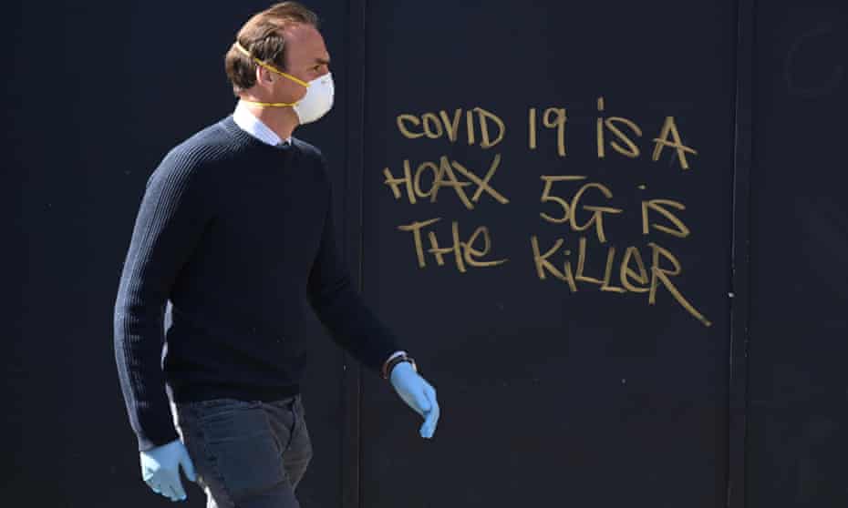 A man in a mask passes 5G conspiracy graffiti in London, Britain