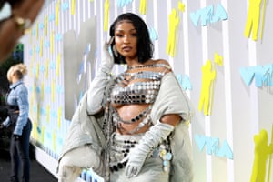 Shenseea is wearing a silver sequinned bra-top with a grey jacket and skirt and elbow-length gloves