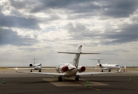 Private jets on the tarmac of Nice international airport. One in the foreground is seen from behind, with two others facing it, forming a geometric pattern with their wings and tailfins. The sky behind them is grey and cloudy.