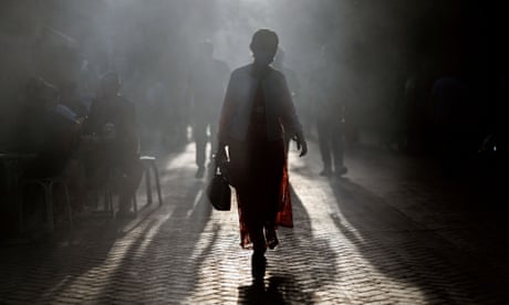 A Uyghur woman through a street silhouetted against the light