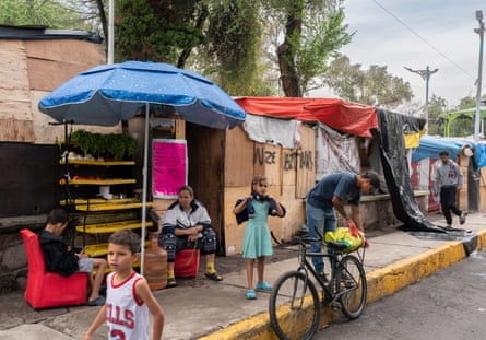 People set up stalls under umbrellas on a roadside, while children mill about.