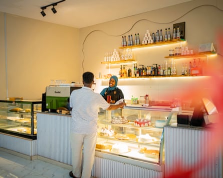 A young somali woman in hijab behind the counter of a coffee shop serving a customer