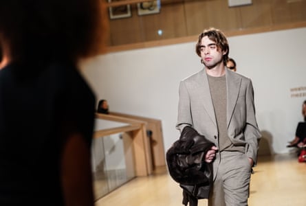 Lennon Gallagher on the catwalk wearing a grey suit and holding a jacket over his arm