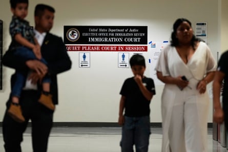 A man holds a child on his hip, and a woman stands with an older child in a hallway.