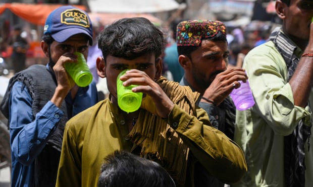 People drink water being distributed by volunteers along a street during a heatwave in Jacobabad on 12 May.