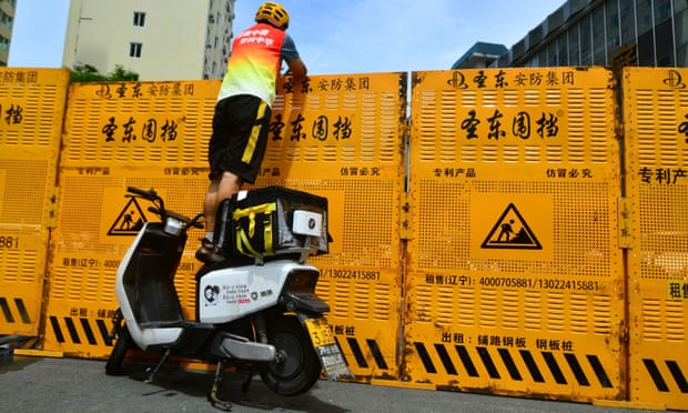 A courier stands on an electric bike to make a delivery over a barricade in Sanya, Hainan province