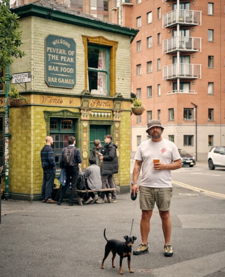A man in hat and shorts with his dog outside Peveril of the Peak pub in Manchester