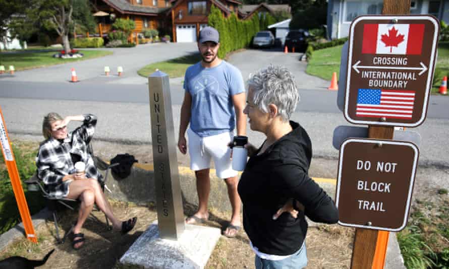 Chelsea Perry, left, and husband Garrick Perry of Calgary, Alberta, meet with friend Alison Gallant of Bellingham, Washington, from opposite sides of the USA-Canada border as the border opens to fully vaccinated Americans while Canadians cannot yet enter the United States for non-essential travel, in Blaine, Washington on 9 August 2021.