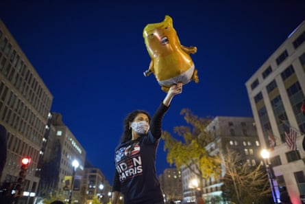 A woman in a Biden-Harris shirt holds a inflated baby Trump doll.